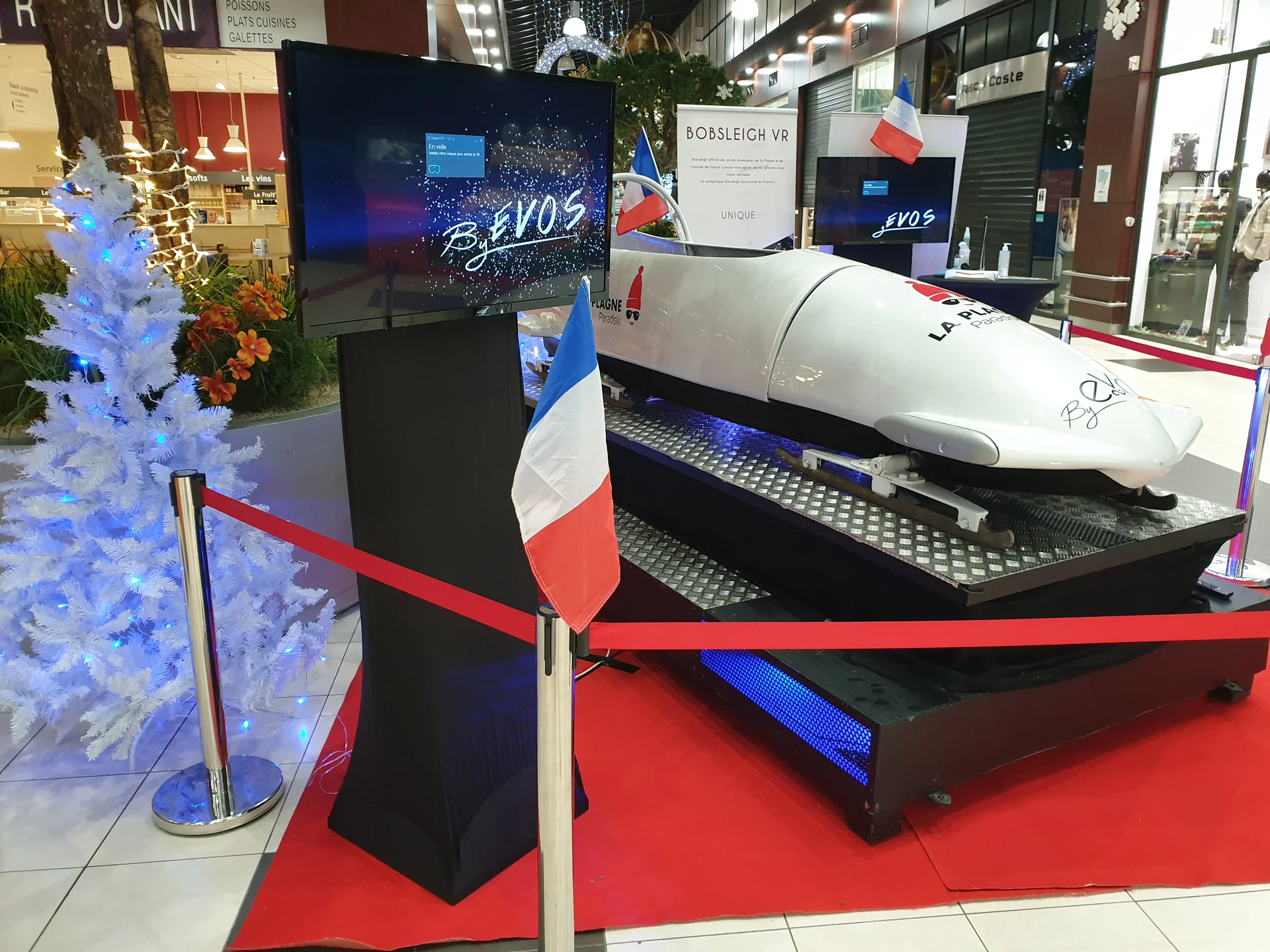 Vue latérale du bobsleigh entre sapin blanc enneigé et drapeau français devant écran de présentation animé
