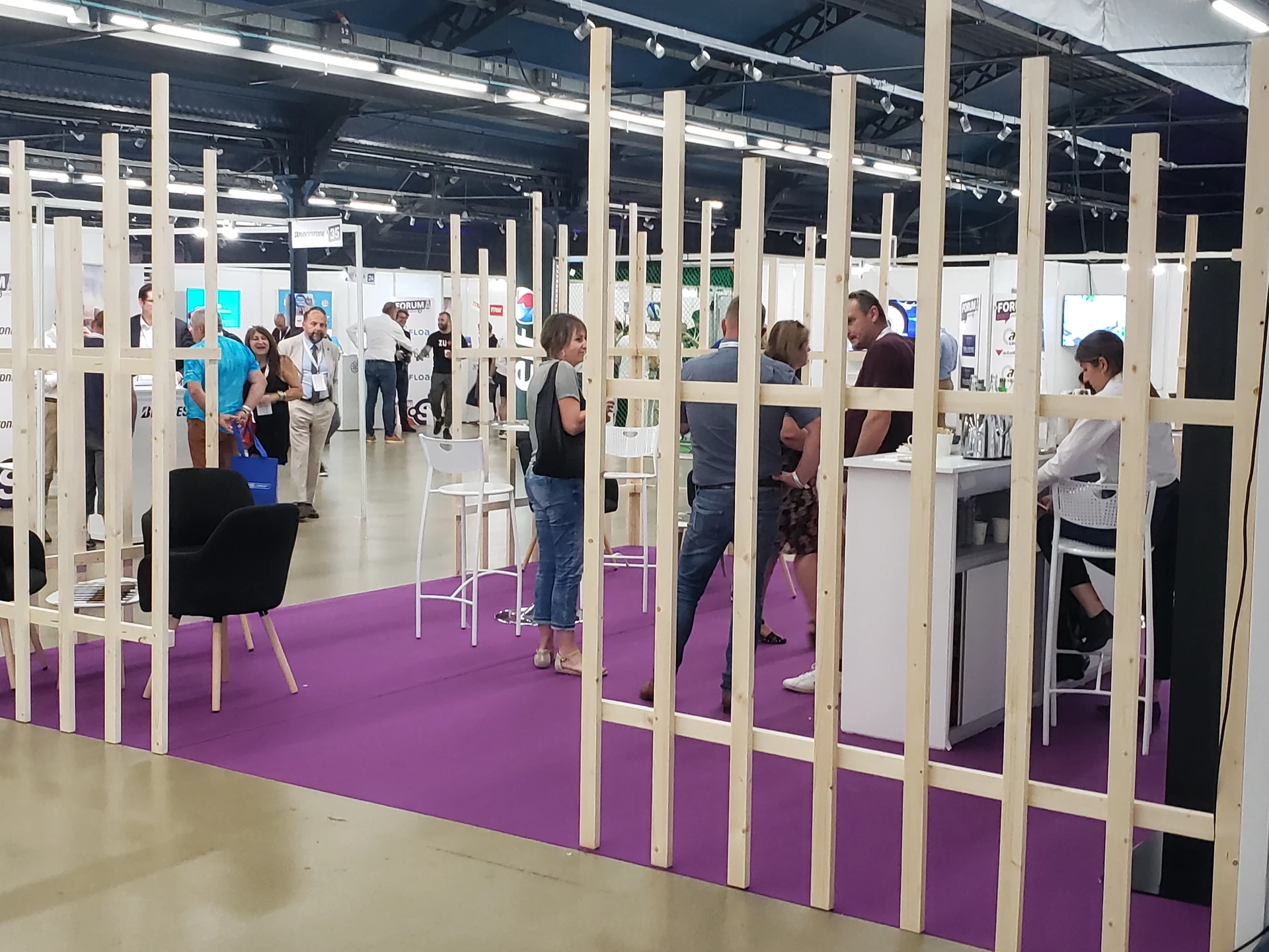 Galerie de stands partenaires en bois clair avec public en circulation au Forum Point S Group 2023