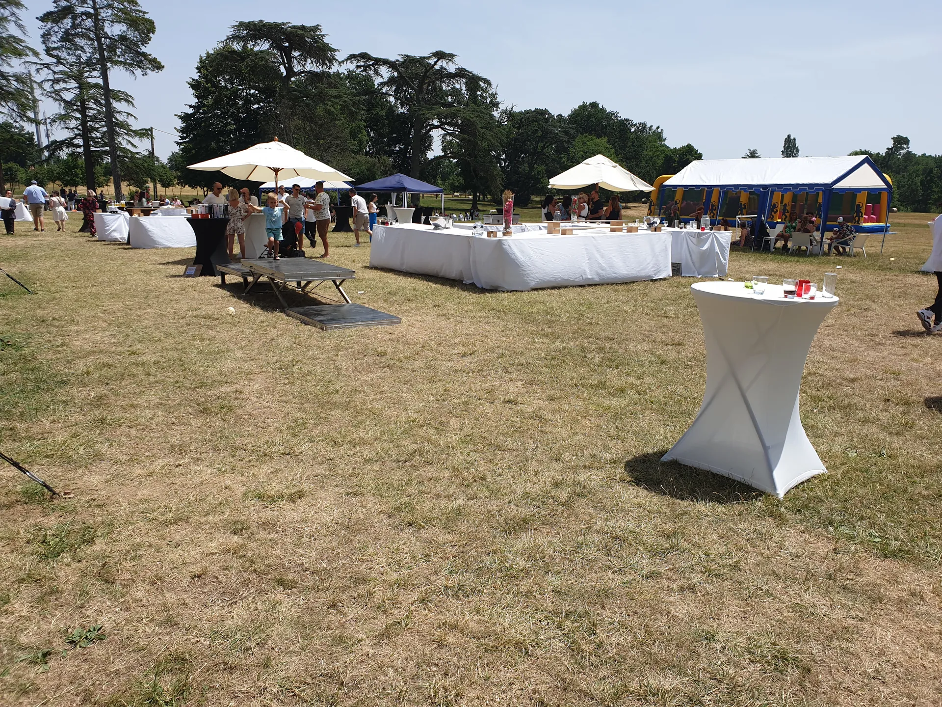 Cocktail dînatoire en plein air sur la pelouse du domaine avec tables hautes et parasols crème