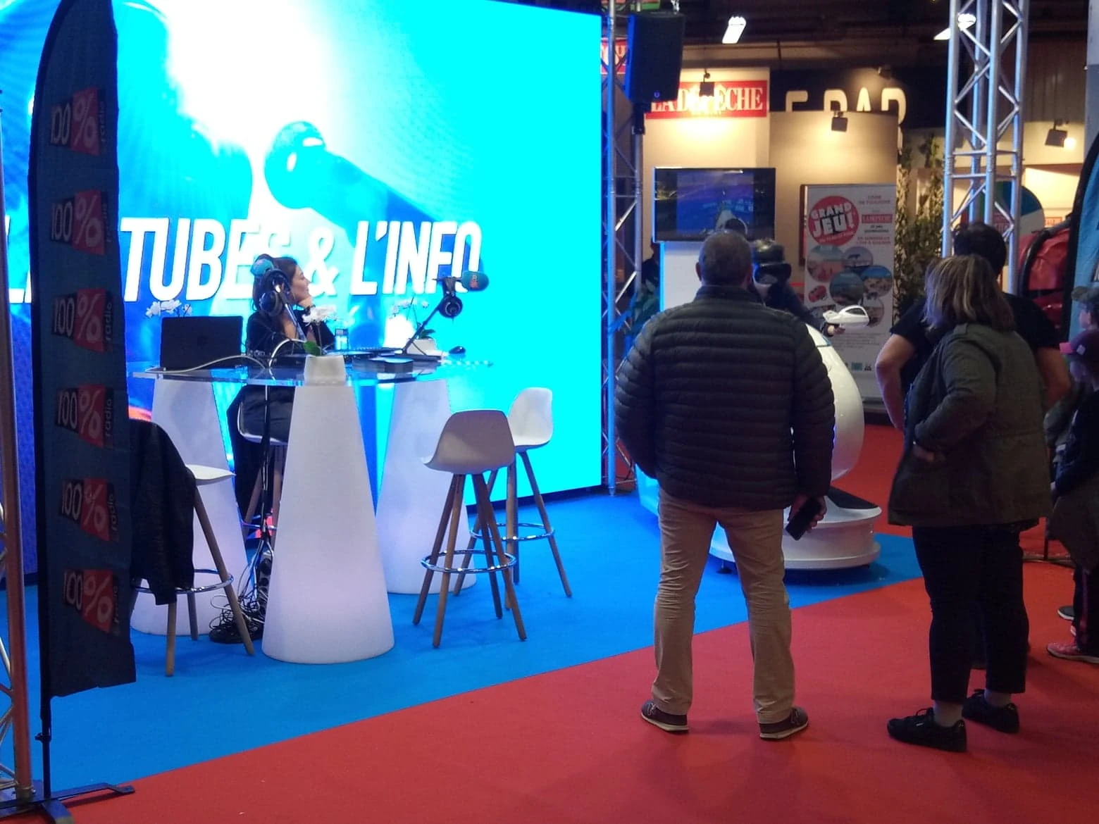 Émission radio Tubes et L'Info en direct sur stand 100% Radio avec simulateur moto VR en arrière-plan