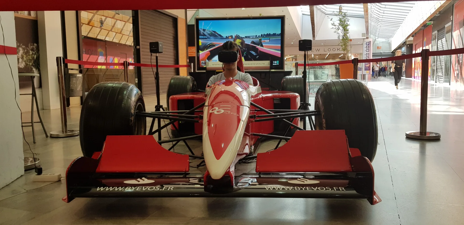 Vue avant du simulateur F1 VR rouge avec branding byevos.fr sur les ailerons en galerie marchande Toulouse