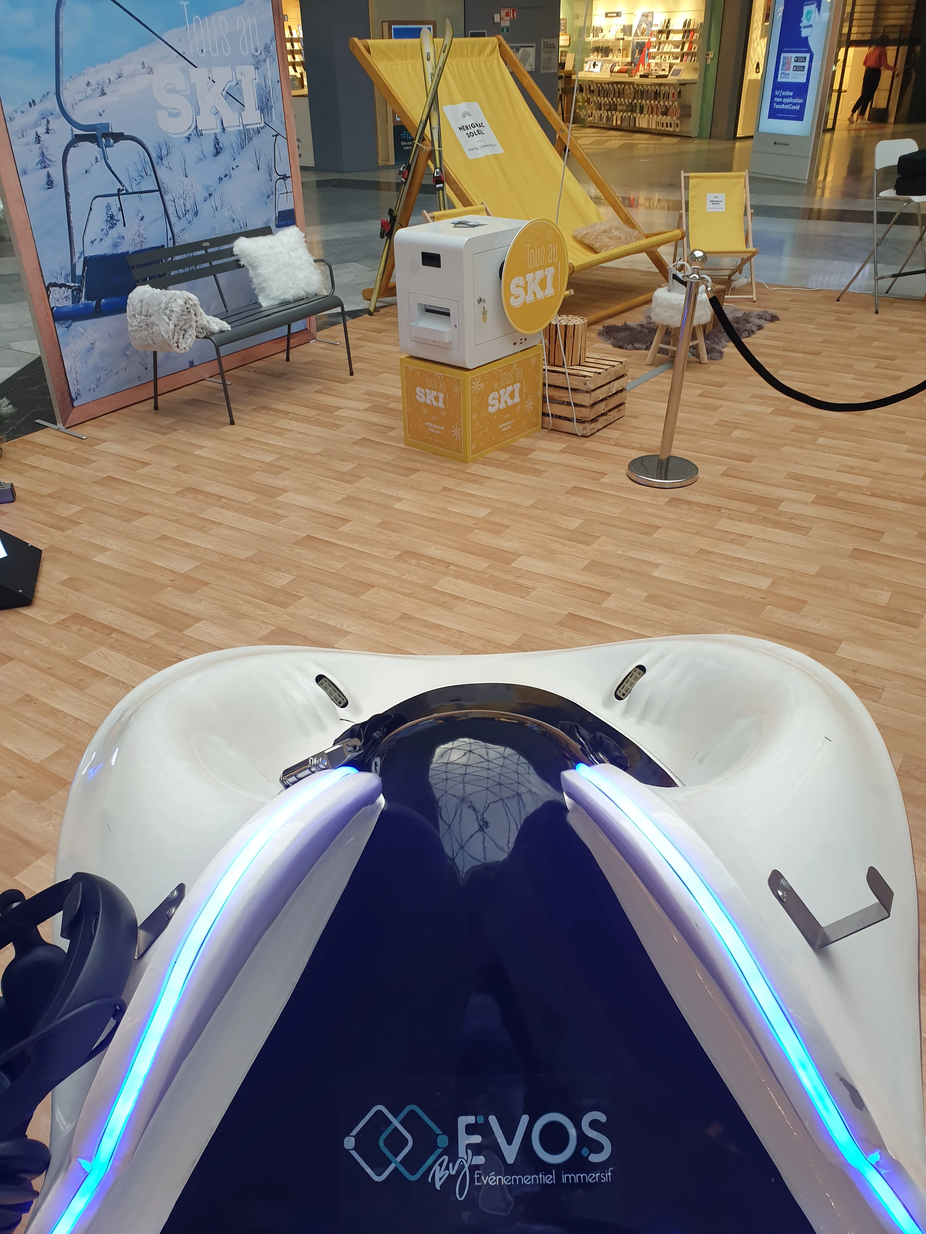 Cockpit simulateur ski VR aux couleurs By Evos en gros plan devant les transats jaunes du décor station