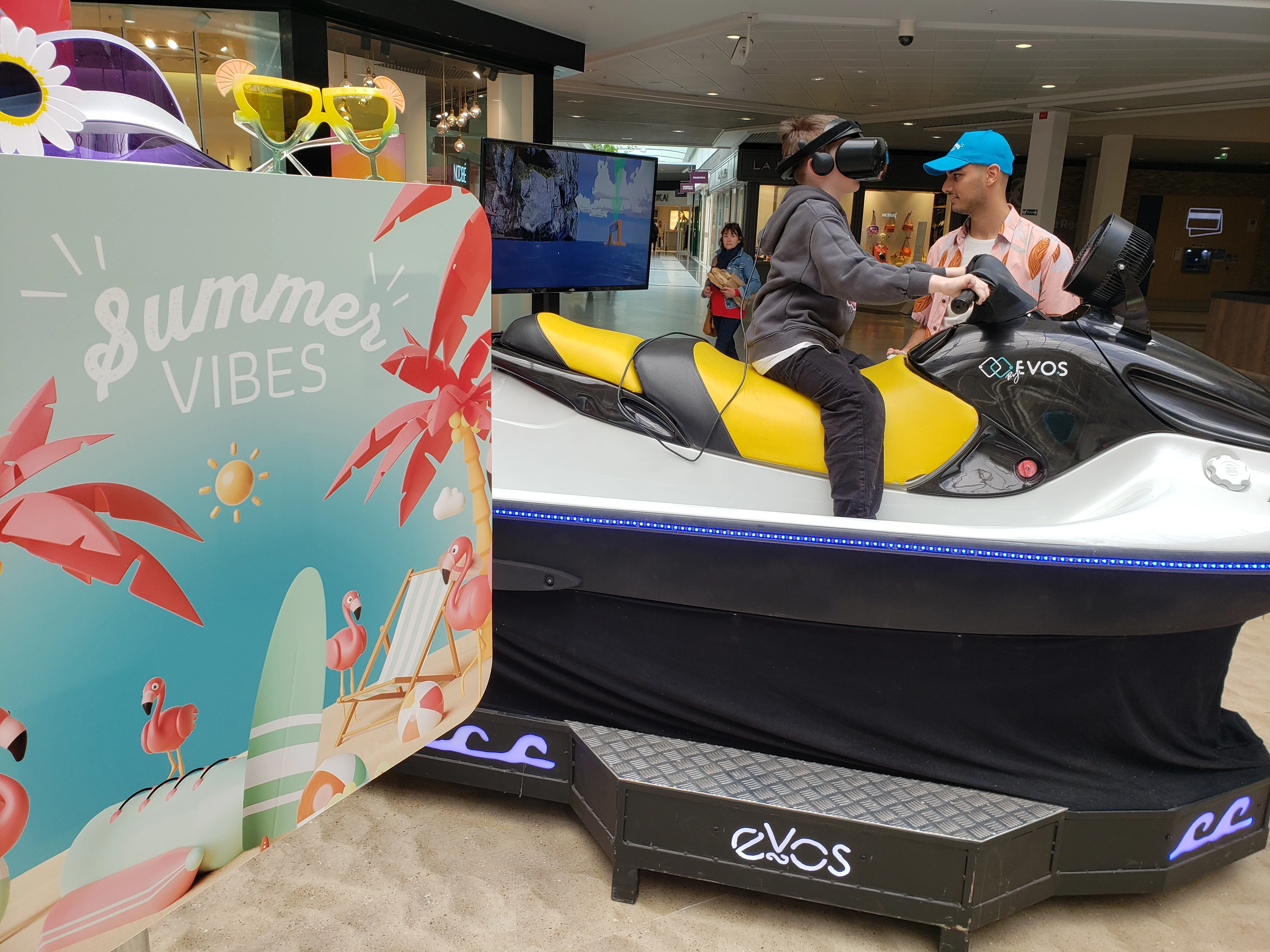 Visiteur sur jet ski VR avec écran de retransmission diffusant les vagues en arrière-plan dans la galerie Mérignac Soleil