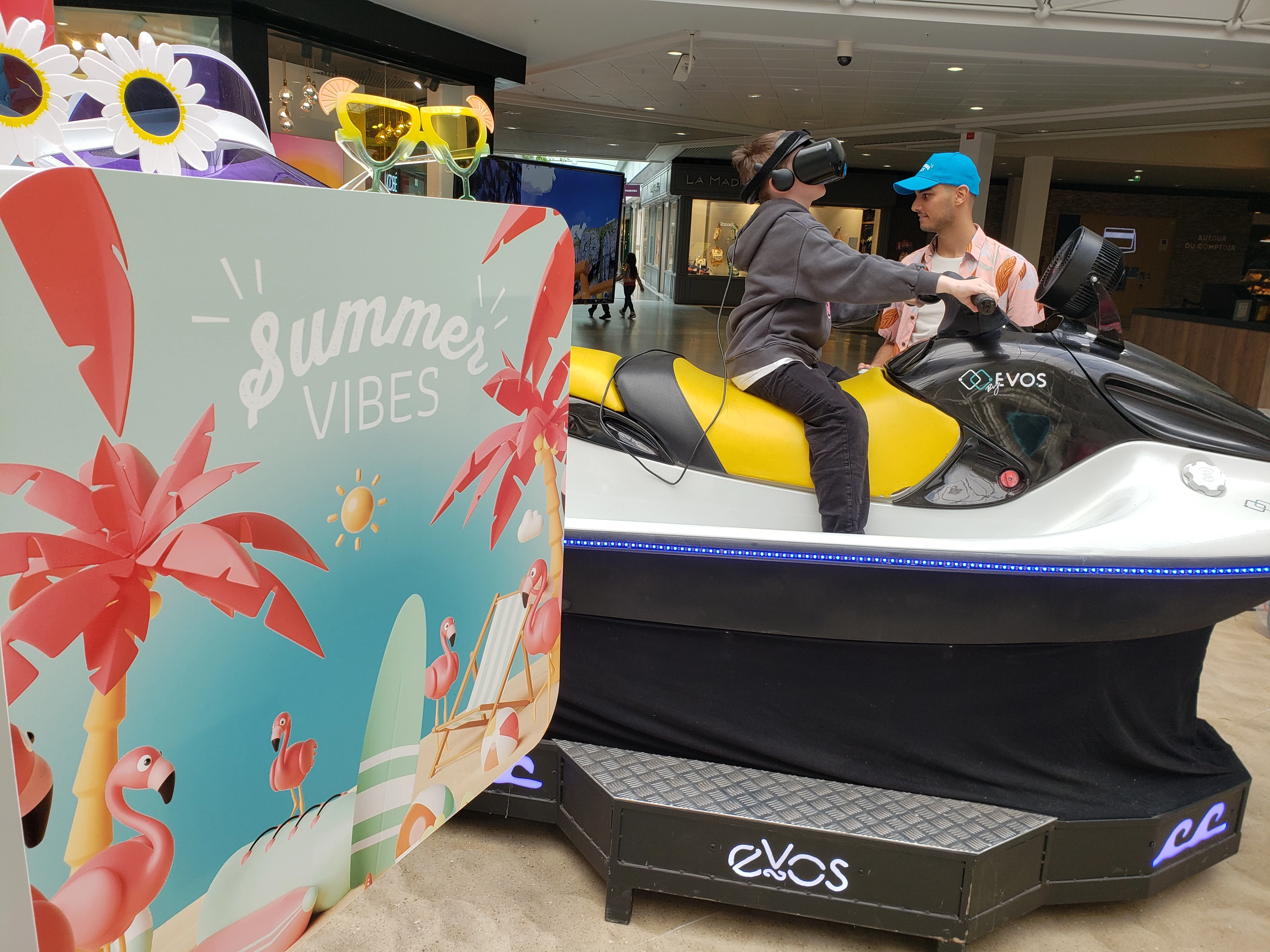 Visiteur casque VR sur le jet ski et surf VR avec décor Summer Vibes palmiers et flamants roses