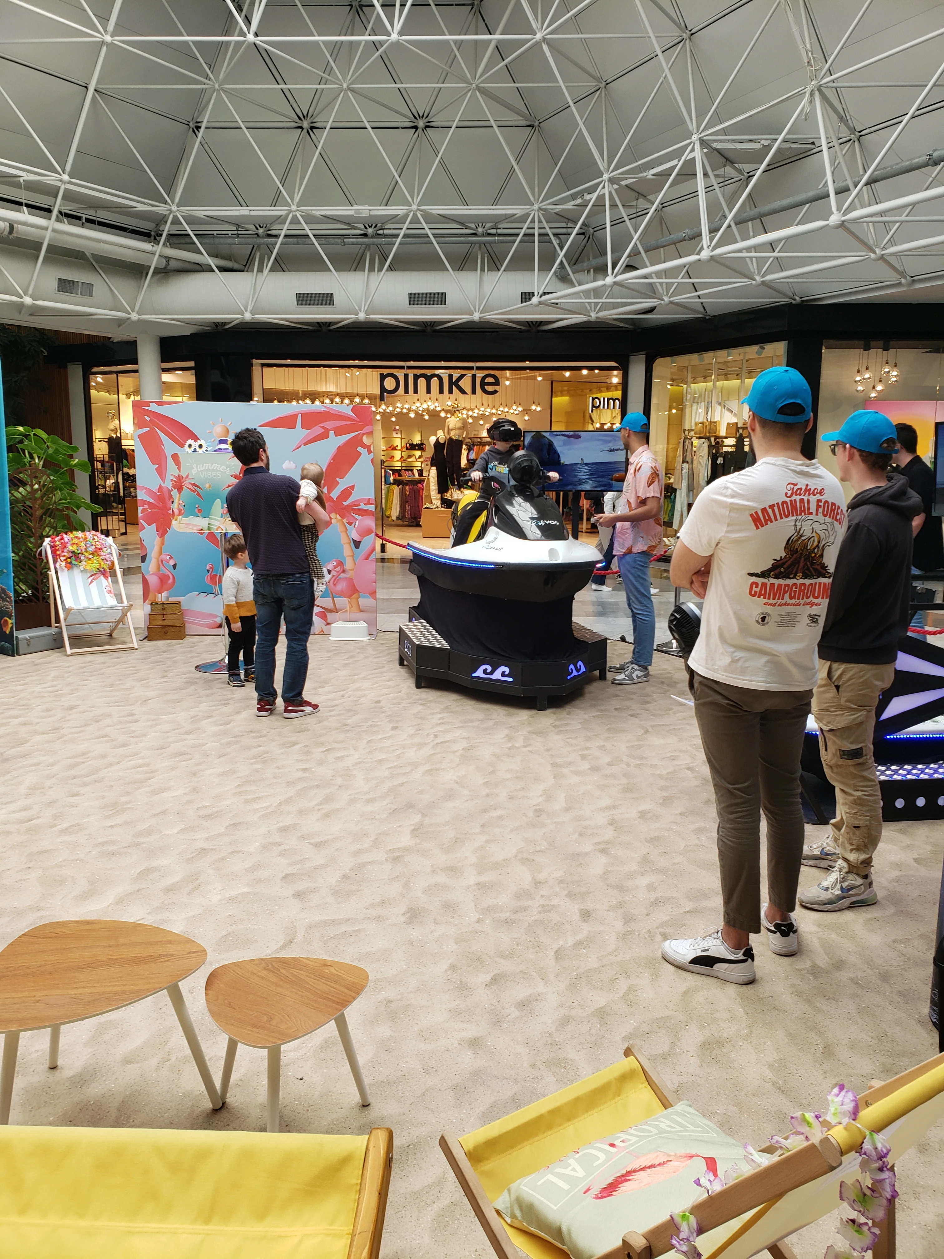 Vue plongée du stand Summer Vibes avec sable au sol et zone d'animation jet ski VR en galerie marchande