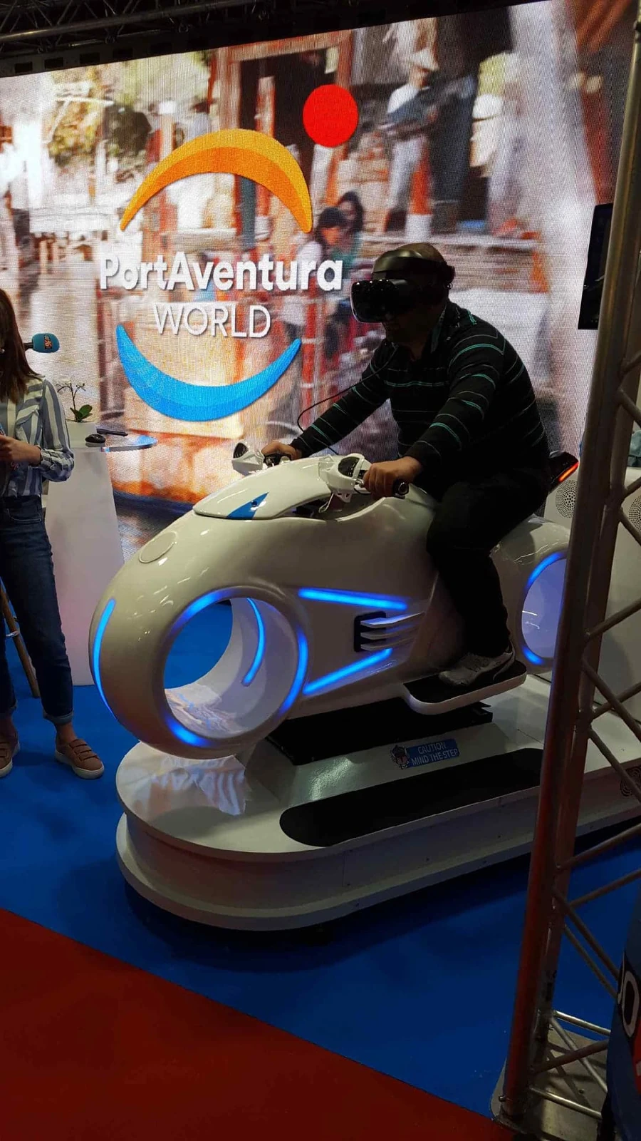 Participant sur simulateur moto VR avec affiche PortAventura World en arrière-plan à la Foire de Toulouse