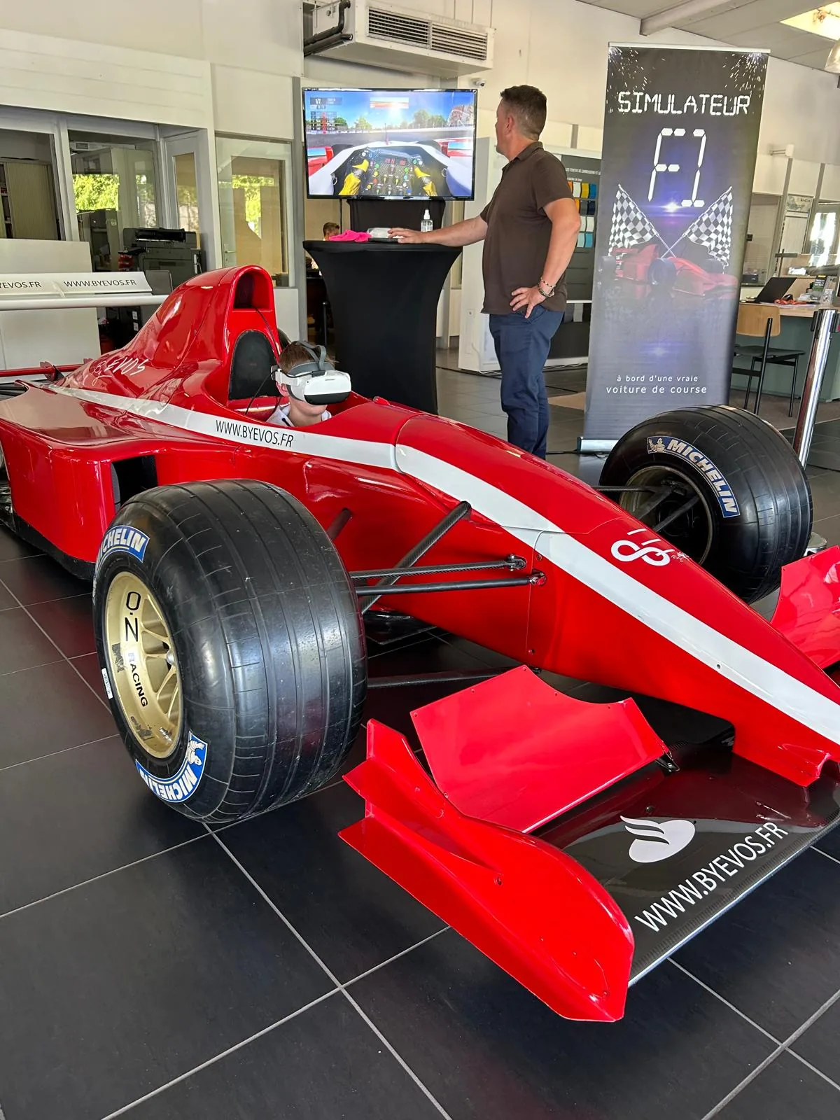 Invité casqué VR au volant du simulateur Formule 1 chez Renault Aurillac avec écran de retransmission visible