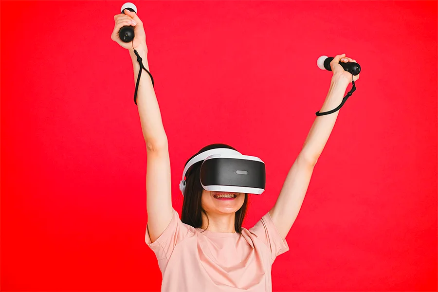 Femme portant un casque VR les bras levés avec des manettes sur fond rouge
