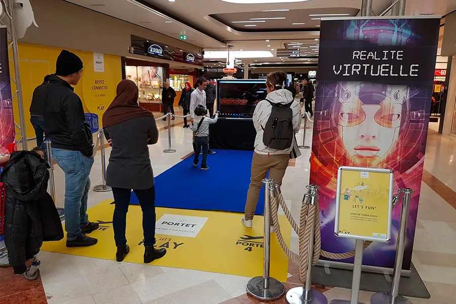 Stand de réalité virtuelle avec panneau et tapis bleu dans une allée de centre commercial