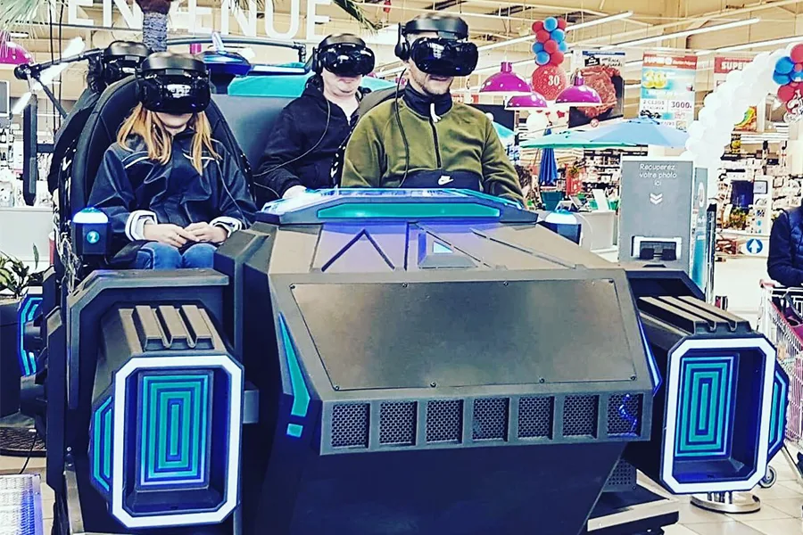 Deux participants assis dans un simulateur VR multijoueur en centre commercial