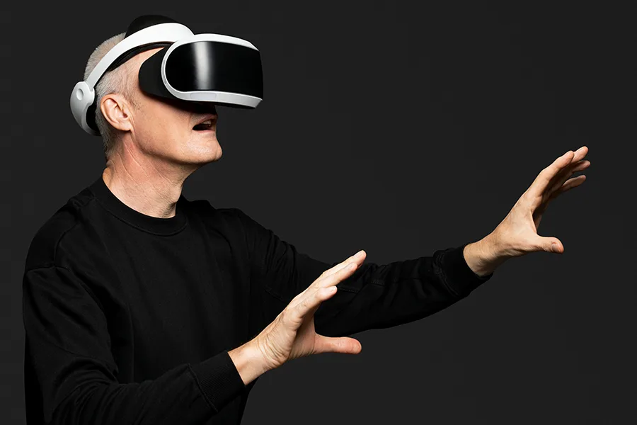 Personne portant un casque de réalité virtuelle et tendant les mains vers un environnement immersif