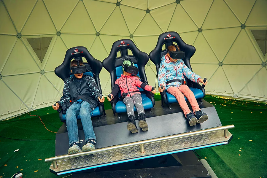 Trois enfants portant des casques VR assis dans un simulateur de vol sous un dôme géodésique