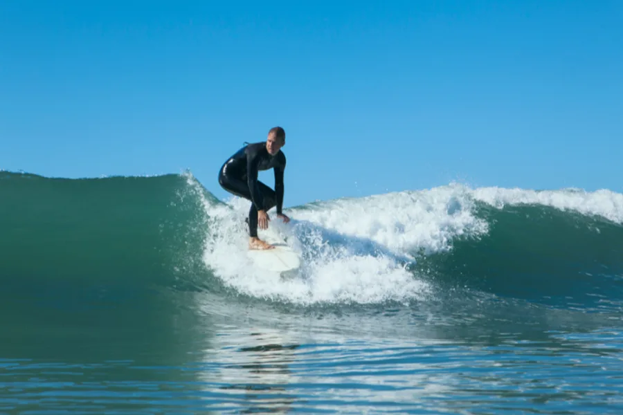 Surfeur en combinaison neoprene sur une vague par ciel bleu