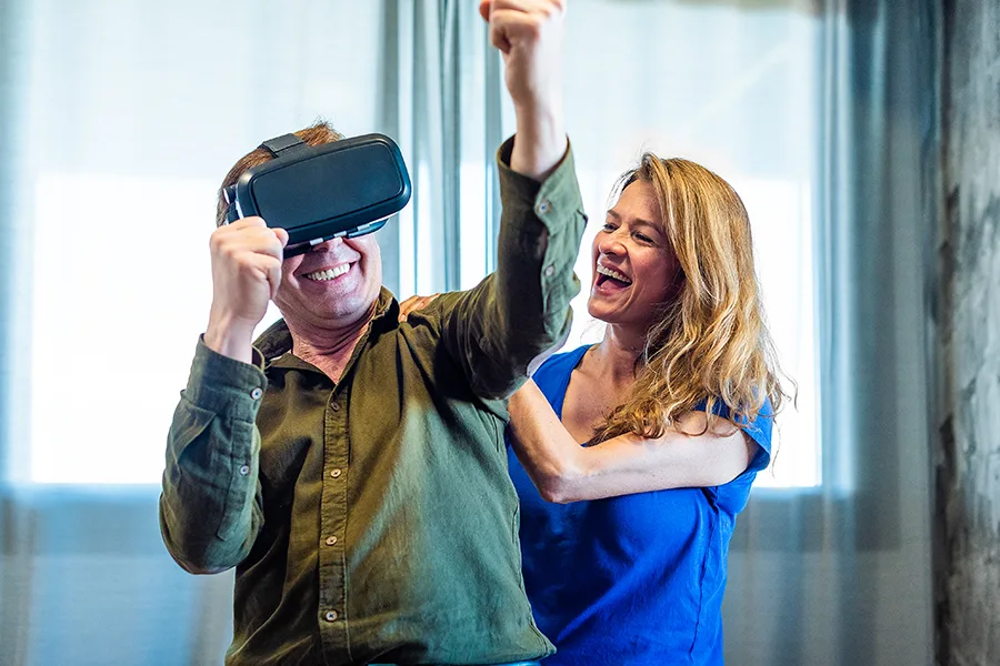 Homme enthousiaste avec un casque VR levant les bras sous le regard amusé d'une accompagnatrice
