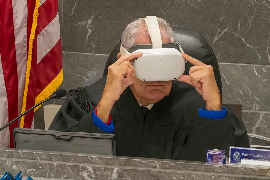 Juge en robe noire ajustant un casque VR blanc sur sa tête, assis devant un drapeau américain